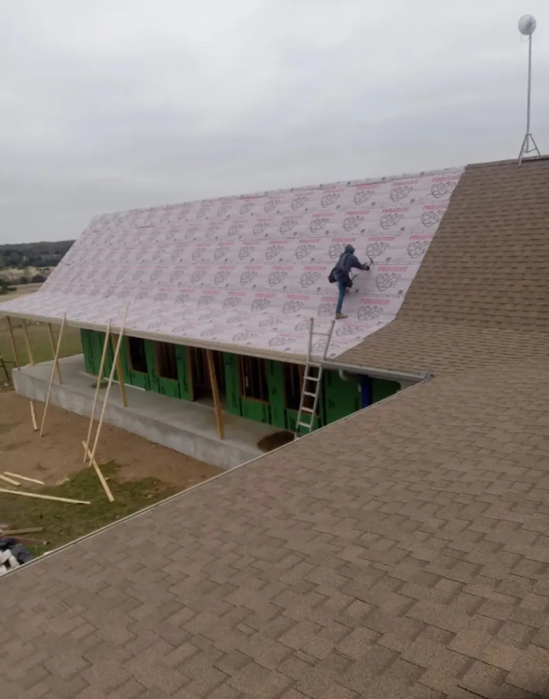Worker preparing underlayment for a metal roof installation in Mason City
